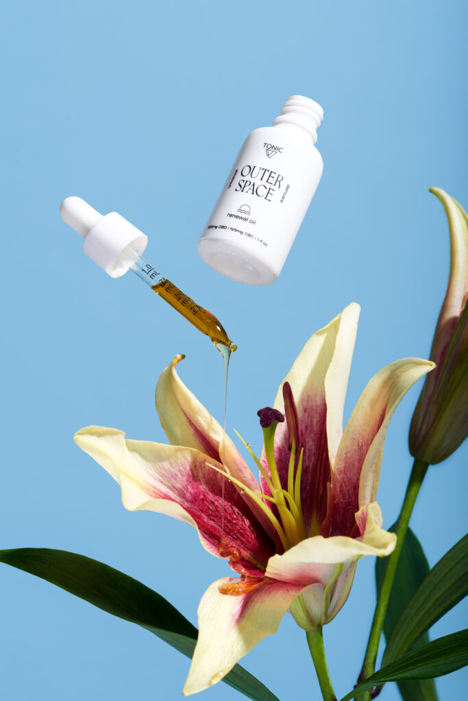 Outer Space Universal Skincare by TONIC Renewal Oil dropping on to flower blue background